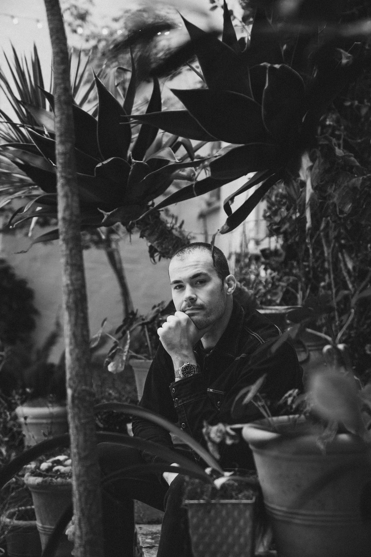 Chris Hall seated among foliage, in black and white